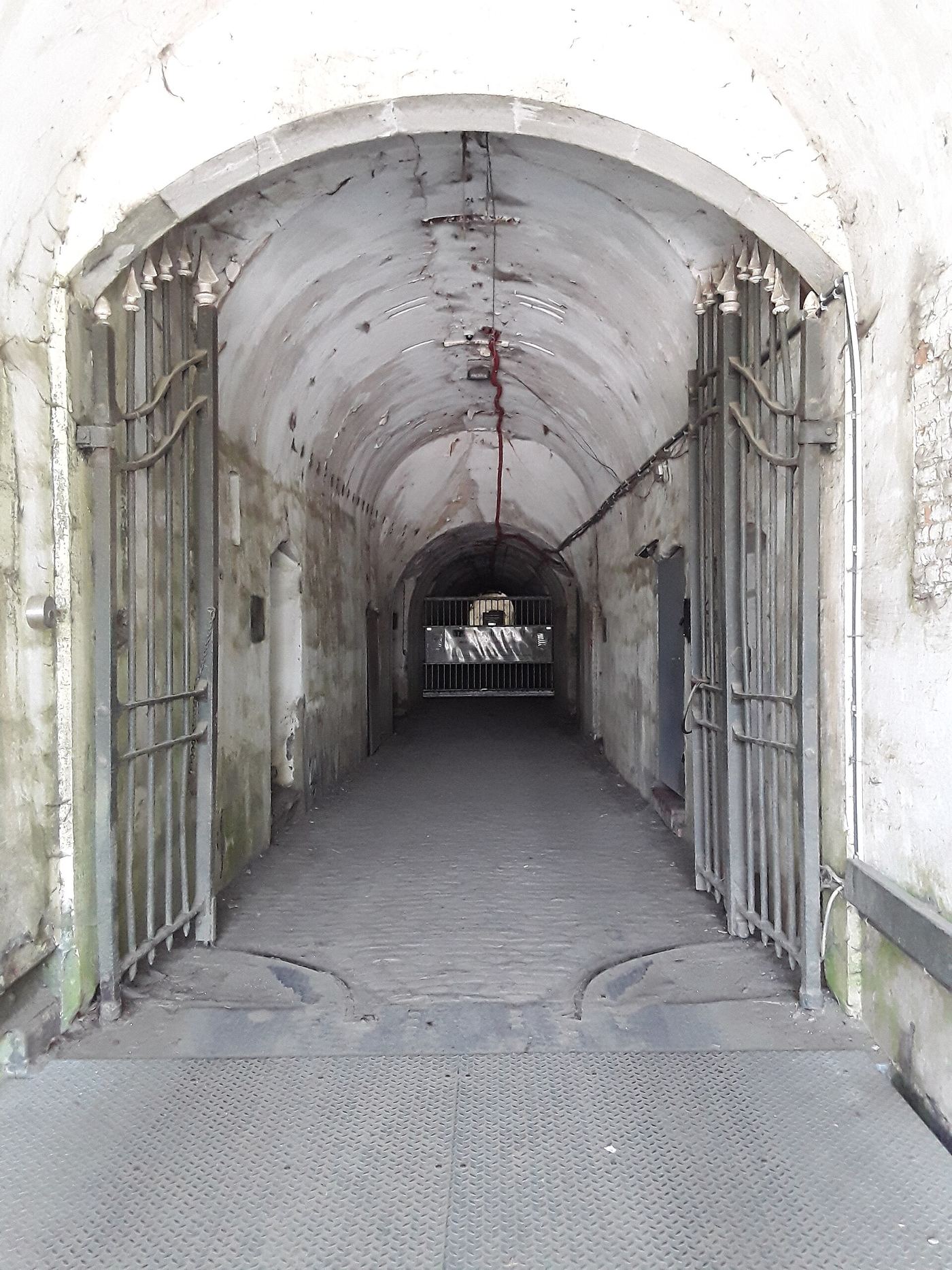 Lange gewelfde gang met witte wanden en een open hek in het fort van Koningshooikt