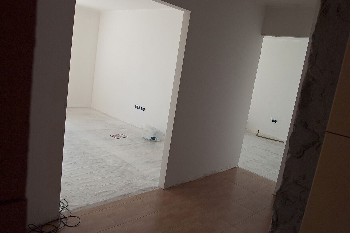 Lege kamer met pas gepleisterde witte muren, een doorgang en een houten vloer